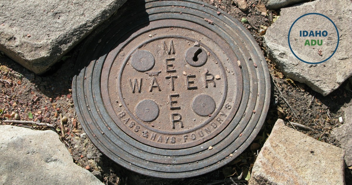 A cast-iron water meter cover set into a stone walkway, the words WATER METER raised across its face