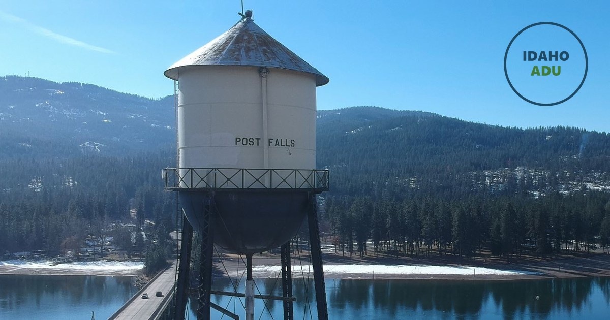 The historic Post Falls water tower above the Spokane River, with forested hills behind it